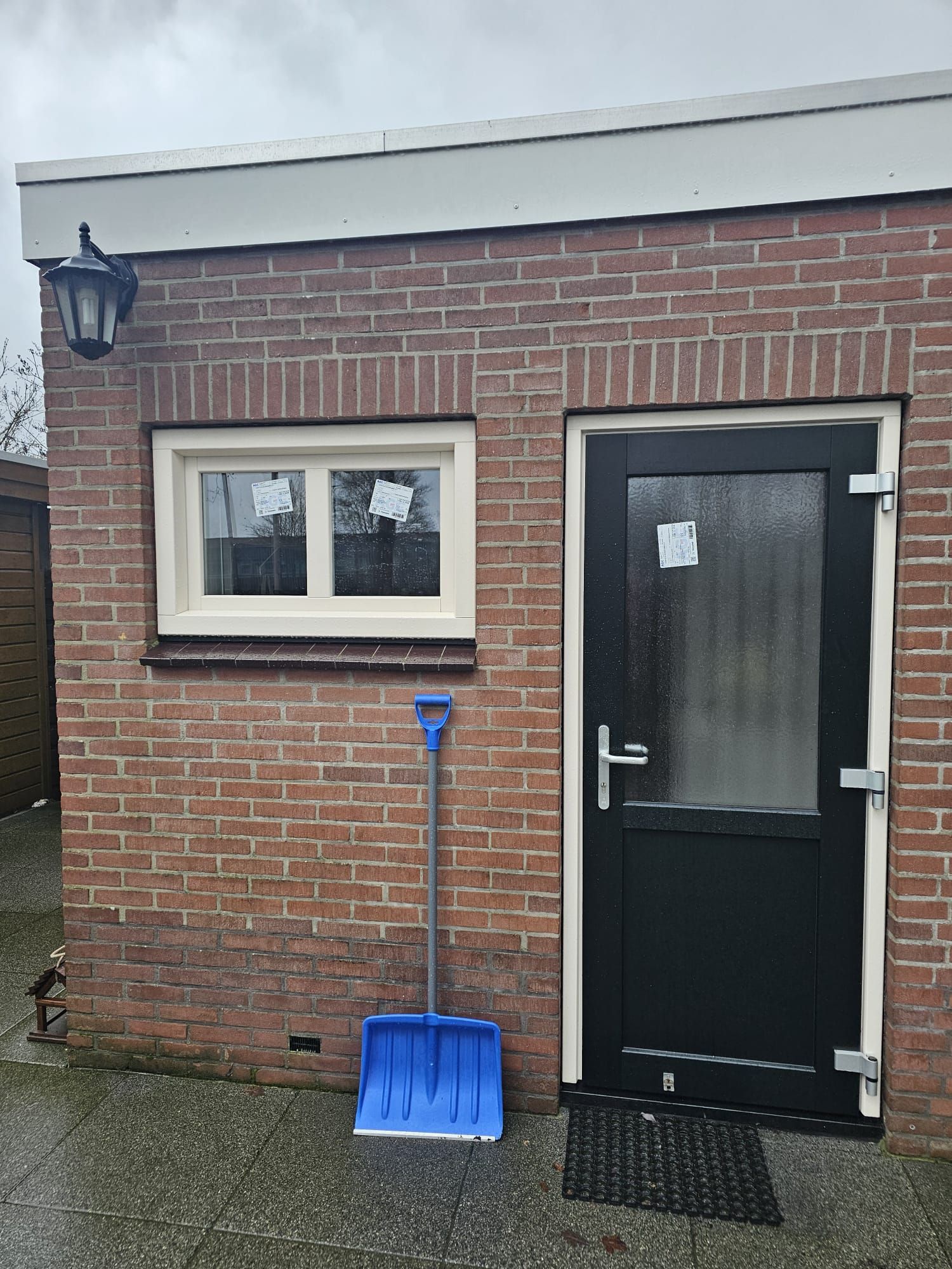 Antraciet kunststof achterdeur naast een wit kunststof raam